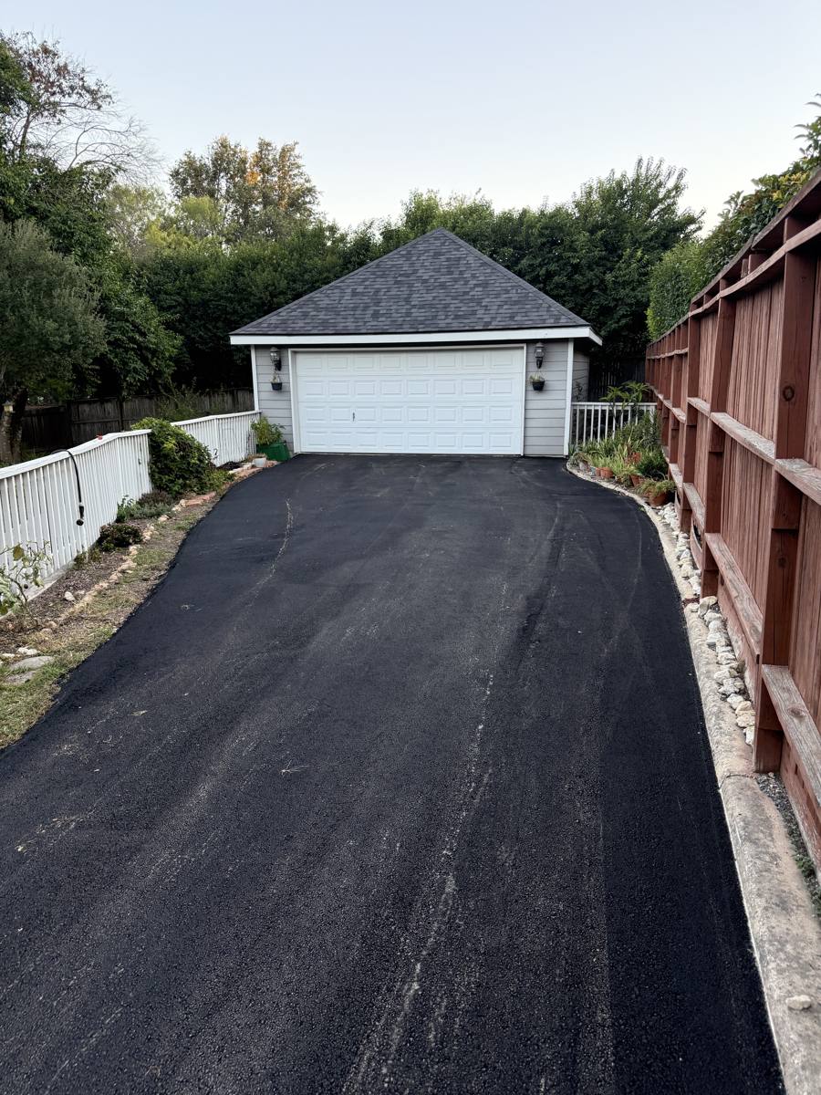 Fresh asphalt driveway leading to a detached garage
